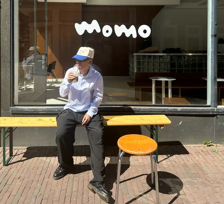 A guest with an iced coffee on the bench outside Café momo, the momo lettering on the window above