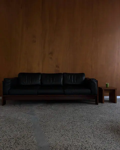 The black leather sofa corner with wood panelling and a terrazzo floor